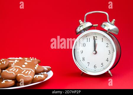 Beautiful vintage silver alarm clock and a plate of gingerbread cookies on a bright red background. Time concept. Holiday routine. Waiting for the hol Stock Photo