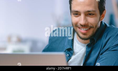 Portrait of a Handsome Young Man Using His Laptop Computer. His Sitting at the Desk in Cozy Living Room. Stock Photo