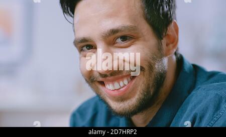 Portrait of Handsome Young Man Using Laptop Computer at Home, Watching into the Camera. Happy Hispanic Man Smiles. Stock Photo