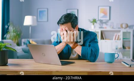 Shot of an Upset Young Man Covers His Face with Palms in Frustration, While Getting Bad News from Reading Bad News on a Laptop. Upset Man at Home. Stock Photo