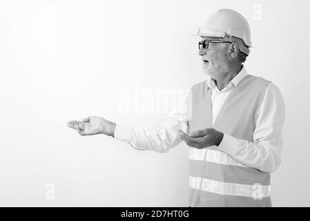 Profile view of handsome senior bearded man construction worker showing something while wearing eyeglasses against white background Stock Photo