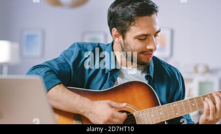 Talented Young Man Plays Guitar While Sitting at His Desk, Reading Chords from a Laptop, Doing Online Video Blogging. Man Practicing Guitar Music Stock Photo