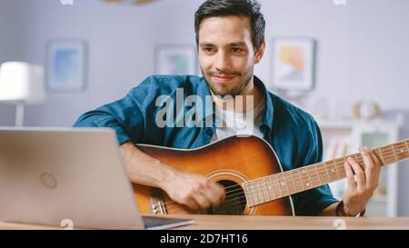 Talented Young Man Plays Guitar While Sitting at His Desk, Reading Chords from a Laptop, Doing Online Video Blogging. Man Practicing Guitar Music Stock Photo