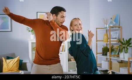 Beautiful Happy Young Couple in Love Dancing in the Middle of the Living Room. Boyfriend and Girlfriend Cheerfully Celebrate by Dancing at Home. Stock Photo