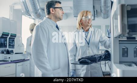 Two Research Scientists Talking about Programming Medical Equipment for Tests. Team of Professionals Doing Pharmaceutical Research in Modern Stock Photo