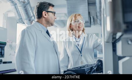 Two Research Scientists Talking about Programming Medical Equipment for Tests. Team of Professionals Doing Pharmaceutical Research in Modern Stock Photo