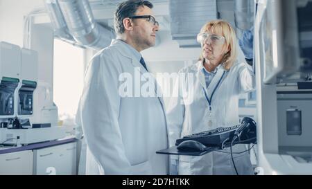 Two Research Scientists Talking about Programming Medical Equipment for Tests. Team of Professionals Doing Pharmaceutical Research in Modern Stock Photo