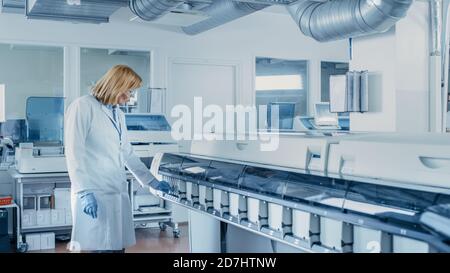 In Laboratory Female Scientist Inspects Medical Equipment Analyzing Test Tube with Blood Samples. Team of Researcher Work in Pharmaceutical Laboratory Stock Photo