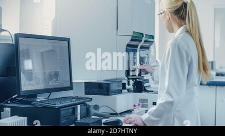 Female Research Scientist Working with Medical Analyzing Machine for Testing Tubes with Blood Sample. Scientist Works in Innovative Pharmaceutical Stock Photo