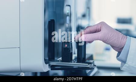 Close-up Female Research Scientist's Hand Holds Test Tube with Blood Sample and Places it Into Medical Analyzing Equipment. Scientist Works in Modern Stock Photo