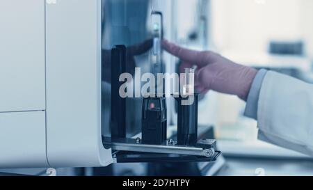 Close-up Female Research Scientist's Hand Pushes the Button for Starting Analyzing Blood Samples in Test Tubes in Medical Analyzing Equipment Stock Photo