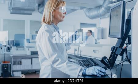 In Laboratory Female Scientist Analyzes Test Tube Data with Blood Samples with Personal Computer. Team of Researchers Work in Pharmaceutical Stock Photo