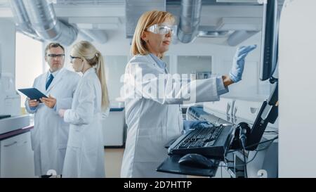 Male and Female Scientists Talking, Using Digital Tablet, Senior Ressearchers Programs Analyzing Equipment. People Working on Genetics Research Stock Photo