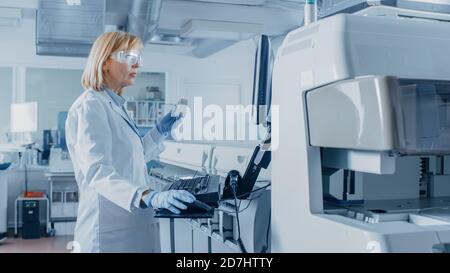 In Laboratory Female Scientist Analyzes Test Tube Data with Blood Samples with Personal Computer. Team of Researchers Work in Pharmaceutical Stock Photo