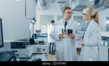 Male and Female Research Scientists Talking, Using Digital Tablet Computer while Working on Genetics Research Project in Innovative Laboratory. Stock Photo