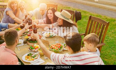 Family and Friends Gathered Together at the Table Raise Glasses and Bottles To Make a Toast and Clink Glasses. Big Family Garden Party Celebration. Stock Photo