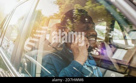 Handsome Young Entrepreneur Traveling on a Passenger Seat of a Car Makes a Phone Call, Talks with Clients or Relatives. Camera Shot from Outside the Stock Photo