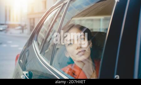 Beautiful Sad Woman Rides on a Passenger Back Seat of a Car, Looks out of the Window Dreamily. Big City View Reflects in the Window. Camera Mounted Stock Photo