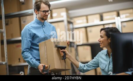 Female Inventory Manager Scans Cardboard Box and Digital Tablet with Barcode Scanner, Male Worker Holds Package. In the Background Rows of Cardboard Stock Photo