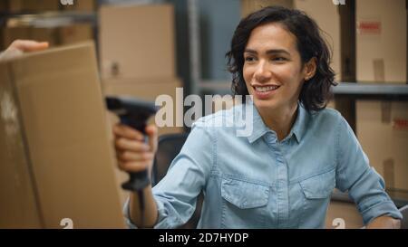 Female Inventory Manager Scans Cardboard Box and with Barcode Scanner, Male Worker Holds Package. In the Background Rows of Cardboard Boxes with Stock Photo