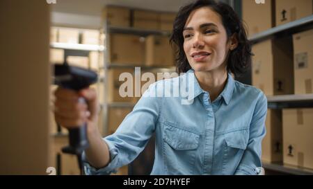 Female Inventory Manager Scans Cardboard Box and with Barcode Scanner. In the Background Rows of Cardboard Boxes with Products Ready For Shipment. Stock Photo