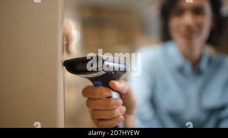 Close-up Shot of Female Inventory Manager Scans Cardboard Box and with Barcode Scanner. In the Background Rows of Cardboard Boxes with Products Ready Stock Photo