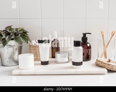 Stylish white bath background with cosmetic bottles, bath accessories and greenhouse plant on white shelf and wall tiles, place for text, bathroom in Stock Photo