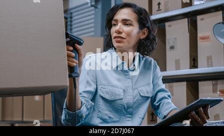 Female Inventory Manager Scans Cardboard Box and Digital Tablet with Barcode Scanner, Worker Holds Package. In the Background Rows of Cardboard Boxes Stock Photo