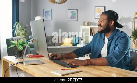 Portrait of the Handsome African American Programmer Working on a Personal Computer while Sitting at His Desk at Home. Stock Photo