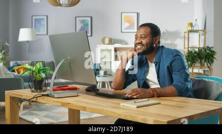 Portrait of the Happy Man Sitting at His Desk, Watching Videos at Home. In the Background Cozy Living Room. Stock Photo