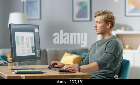 Handsome Focused Young Man Works on a UX UI Mobile App Template, Uses Personal Computer while Sitting at His Desk in the Cozy Apartment. Stock Photo