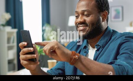 Portrait of the Handsome Young Man Using Smartphone, Browsing in Internet, Checking Social Networks, Scrolling Newsfeed while Sitting At Home. Stock Photo