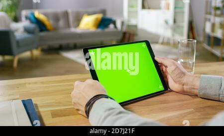 Man Holding Green Mock-up Screen Digital Tablet Computer While Sitting at the Desk. Man Buying stuff or Browsing Through the Internet. In the Stock Photo