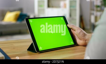 Man Watching Green Mock-up Screen Digital Tablet Computer While Sitting at the Desk. Man Watching Videos or Browsing Through the Internet. In the Stock Photo
