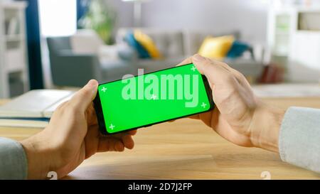 First Person Close-up of the Man Holding Green Screen Smartphone in Landscape Mode and Playing in a Racing Video Game by Tilting Mobile Phone Stock Photo