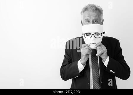 Studio shot of handsome senior bearded businessman hiding behind white mask with eyeglasses against white background Stock Photo