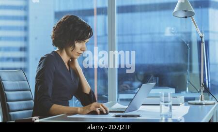 Side View Portrait of the Beautiful Businesswoman Working on a Laptop in Her Modern Office with Cityscape Window View. Female Executive Uses Computer. Stock Photo