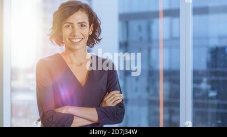 Portrait of the Successful Hispanic Businesswoman Crossing Her Arms and Smiling. Beautiful Female Executive Standing in Her Office. Summertie Flares. Stock Photo