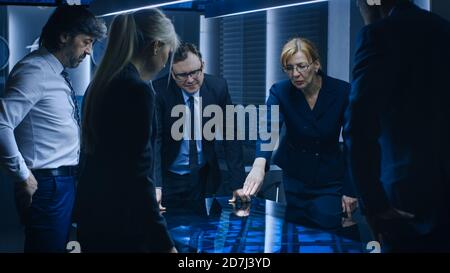 Diverse Team of Government Intelligence Agents Standing Around Digital Touch Screen Table and Tracking Suspect, Senior Officer does Interactive Stock Photo