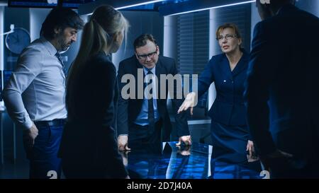 Diverse Team of Government Intelligence Agents Standing Around Digital Touch Screen Table and Tracking Suspect, Senior Officer does Interactive Stock Photo