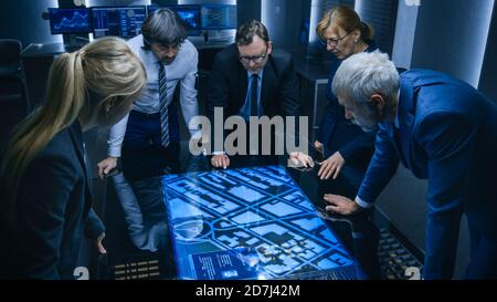 High Angle Shot of Team of Government Intelligence Agents Talking while Standing Around Digital Touch Screen Table and Tracking Suspect. Satellite Stock Photo
