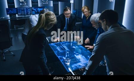 Team of Government Intelligence FBI Agents Standing Around Digital Touch Screen Table and Tracking Suspect Vehicle Using Satellite Surveillance in the Stock Photo