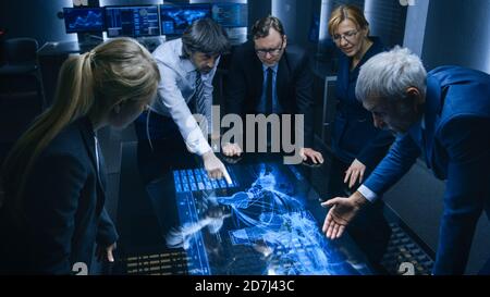 Team of Government Intelligence FBI Agents Standing Around Digital Touch Screen Table and Tracking Suspect Vehicle Using Satellite Surveillance in the Stock Photo