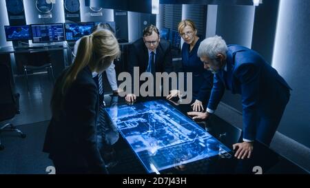 Team of Government Intelligence FBI Agents Standing Around Digital Touch Screen Table and Tracking Suspect Vehicle Using Satellite Surveillance in the Stock Photo