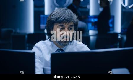 Professional Operators Working On Computers in System Control Room. Secret Government Agency Analysts Doing Research, Conducting Cyber Security Stock Photo