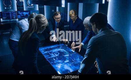 Team of Government Intelligence FBI Agents Standing Around Digital Touch Screen Table and Tracking Suspect Vehicle Using Satellite Surveillance in the Stock Photo