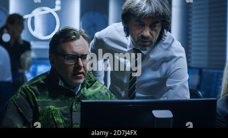 Military Dispatcher Wearing Headset Talks with Homeland Security Official in the System Control Monitoring Room.  Stock Photo