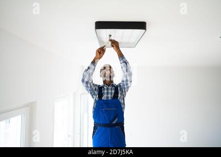 African Maintenance Electrician On Ladder Fixing And Installing Light Stock Photo
