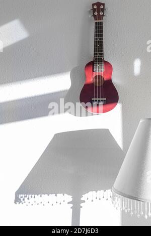 Red Ukulele on the white wall in the morning sunlight Stock Photo