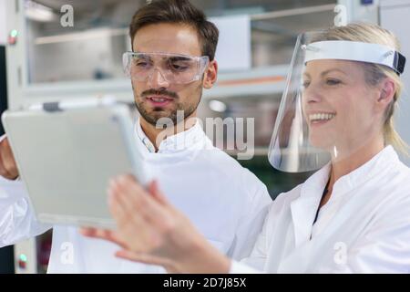 Male and female technicians discussing over digital tablet at illuminated laboratory Stock Photo